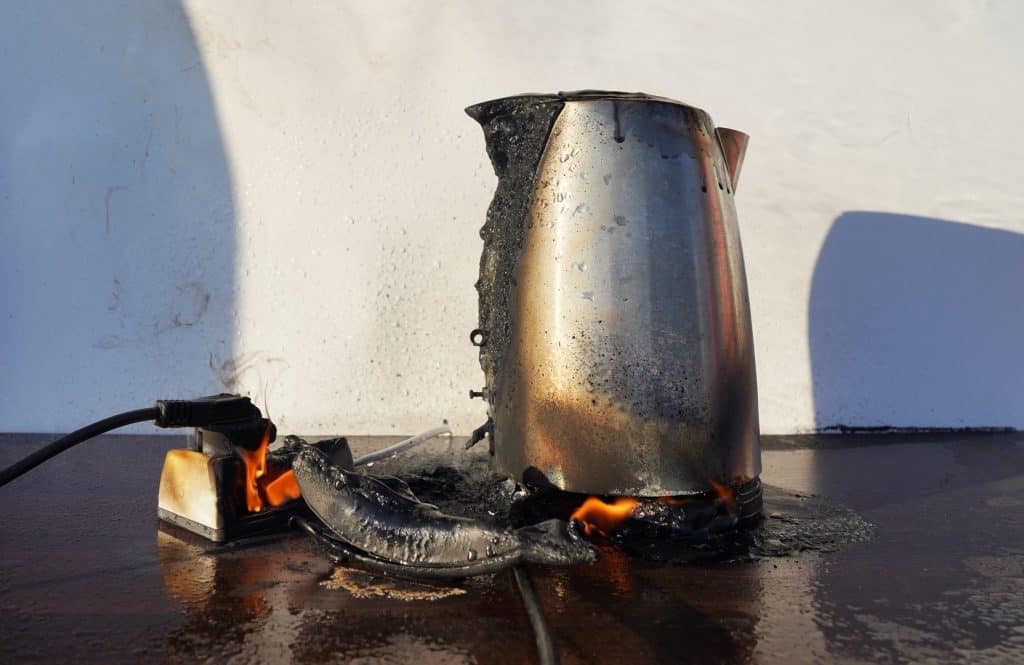 Chaleira elétrica em chamas. Chaleira elétrica para chá pegou fogo sobre a mesa. A chaleira elétrica derreteu devido a um curto-circuito na fiação elétrica. Corrente elétrica sobrecarregada ou curto no dispositivo.