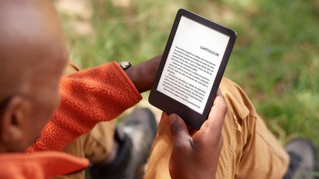 Como usar o Kindle para aprender um novo idioma? Que tal juntar sua paixão por ler com a chance de aprender um novo idioma? Com o Kindle, você pode unir sua paixão pela leitura ao aprendizado de uma nova língua. O queridinho por quem valoriza praticidade e o acesso a uma vasta biblioteca em um só lugar, se torna uma poderosa ferramenta de estudo e descoberta. Homem lendo num Kindle num parque