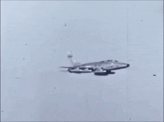 Um caça bombardeiro North American F-100 Super Sabre despejando bombas, do tipo BLU, contendo Napalm, em um exercício de treinamento.