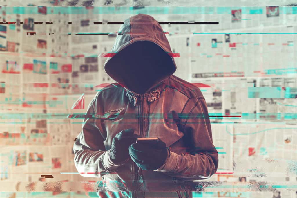 Pessoa com um capuz cobrindo cabeça e rosto com um celular nas mãos