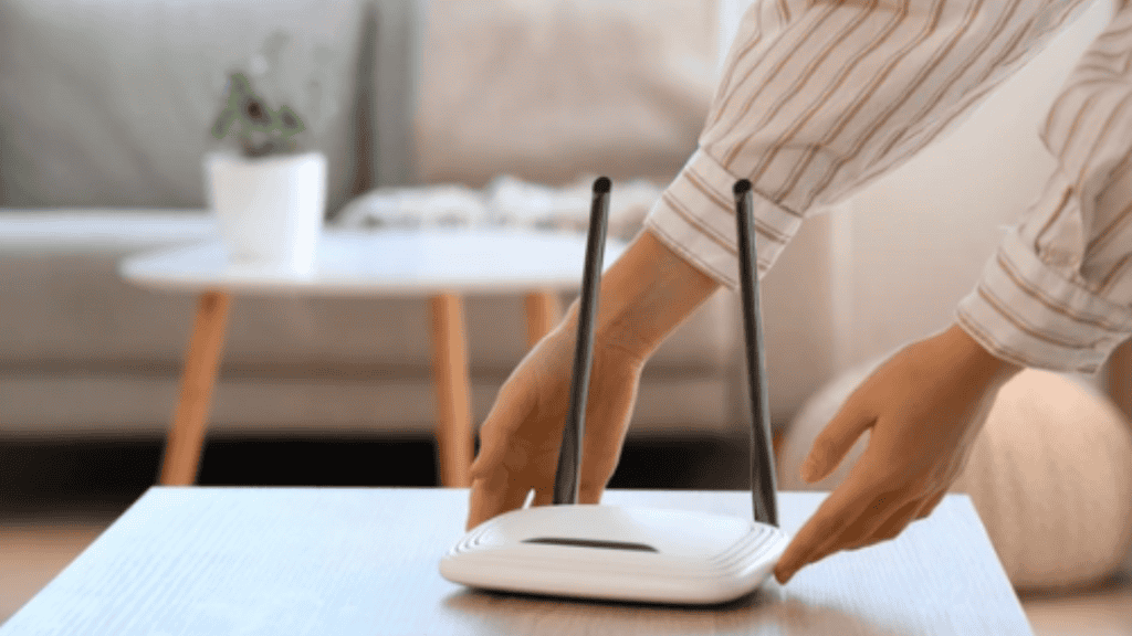 Roteador Wi‑Fi: 6 erros que encurtam a vida útil dele (e como evitar) Se o Wi‑Fi vive caindo, o sinal oscila ou o roteador esquenta demais, a dor de cabeça e o gasto com troca de equipamento chegam rápido. mulher colocando roteador em cima de mesa em um ambiente de sala
