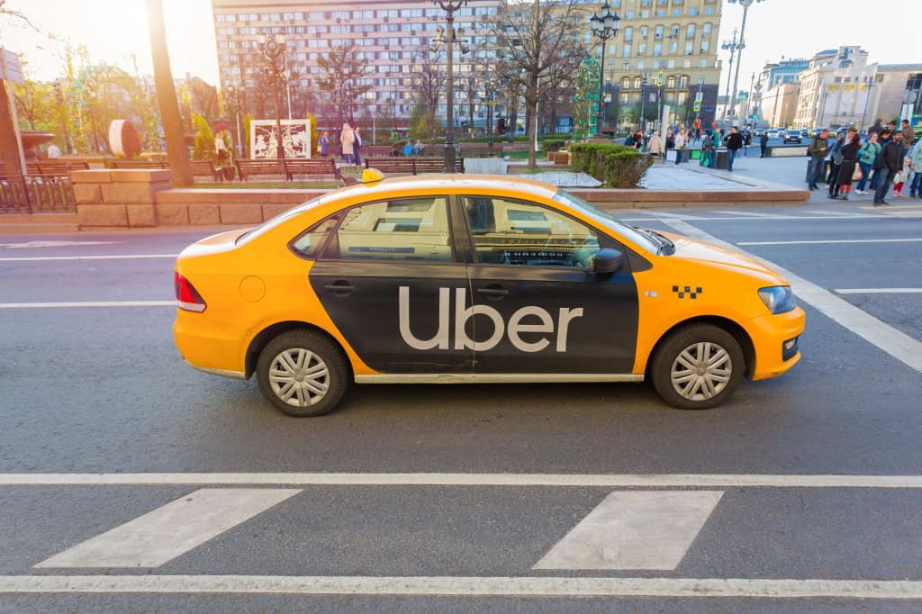 Taxí amarelo com logo preto na lateral da Uber.