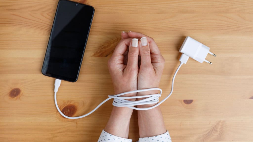 Vício em celular? 5 possíveis sintomas para ficar de olho As informações presentes neste texto têm caráter informativo e não substituem a orientação de profissionais de saúde. Consulte um médico ou especialista para avaliar o seu caso. Mãos de mulher amarradas nos pulsos com cabo de celular como algemas. Vício em redes sociais