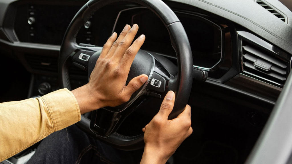 Jovem negro buzinando enquanto dirige, sentado no carro, segurando o volante, apitando a buzina no carro
