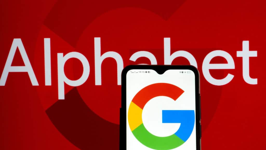 Google fica a um passo dos US$ 3 trilhões após vitória em julgamento sobre monopólio Após um juiz federal dos EUA decidir que o Google não precisava vender o Chrome nem o Android no julgamento sobre monopólio, as ações da Alphabet subiram 10%. Isso colocou a big tech bem perto de atingir o valor de mercado de US$ 3 trilhões. Celular com logotipo do Google na tela colocado na frente de uma tela exibindo letreiro escrito Alphabet