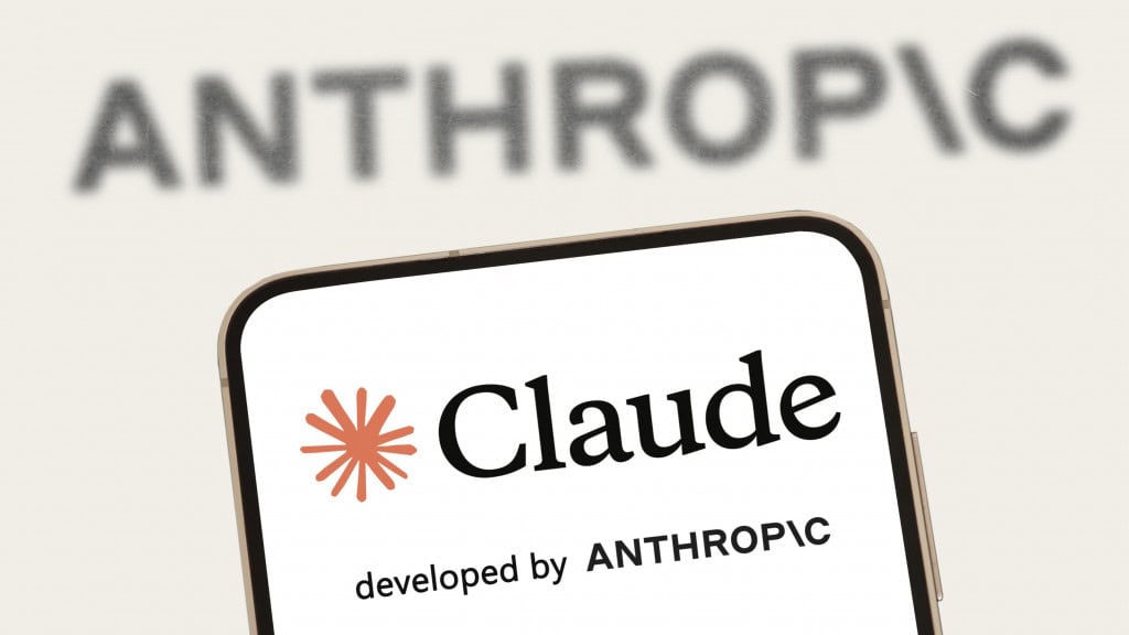 Celular com logotipo do Claude na tela na frente de tela maior exibindo letreiro no qual está escrito Anthropic