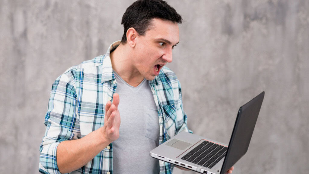 Rapaz olha o Notebook com raiva e ameça dar um tapa