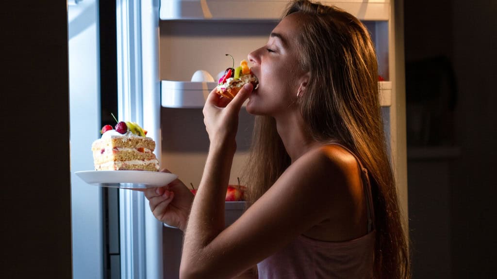 Jantar tarde da noite, pouco antes de dormir, pode prejudicar a saúde? O hábito de jantar tarde da noite, especialmente pouco antes de dormir, é bastante comum entre pessoas com rotinas intensas de trabalho, estudo e compromissos. Muitas vezes, as refeições acabam sendo adiadas para depois das 21h. Mas será que esse costume pode prejudicar a saúde? Mulher comendo bolo tarde da noite