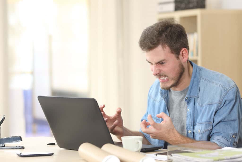 6 erros que deixam o processador do Windows mais lento e como resolvê-los É uma situação frustrante quando você está trabalhando, jogando ou simplesmente navegando na internet e, de repente, o PC Windows começa a travar. Os programas ficam lentos, o cursor do mouse move-se aos trancos e a ventoinha do computador começa a zumbir como se estivesse decolando. Imagem mostra homem irritado e furioso com um laptop em um pequeno escritório ou casa