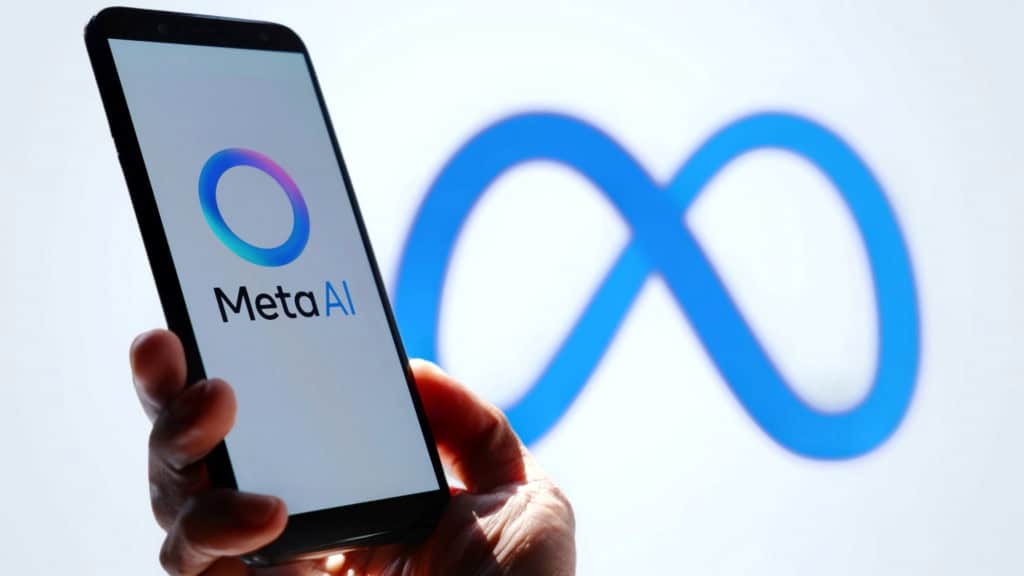 Ao fundo, meio desfocado, o logo da Meta; à frente e à esquerda, uma pessoa segura um smartphone em pé, no qual se vê o logo da Meta AI