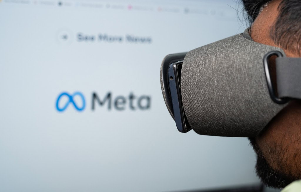 Meta desafia Apple com novos óculos de IA A Meta, controladora do Facebook e Instagram, continua investindo pesado em hardware e inteligência artificial, mesmo com prejuízos expressivos. Ao fundo, desfocado, logo da Meta contrastando com o rosto de uma pessoa quase de perfil e com um óculos e realidade virtual