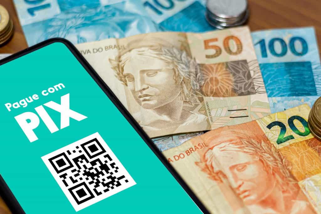 Pix ganha hoje botão de contestação; saiba como usar Nesta quarta-feira (1), o Pix passou a contar com nova função: o “botão de contestação” para casos de fraude, golpe e coerção, segundo o Banco Central (BC). Smartphone com os dizeres "Pague com PIX" e um QR Code em cima de várias notas de real