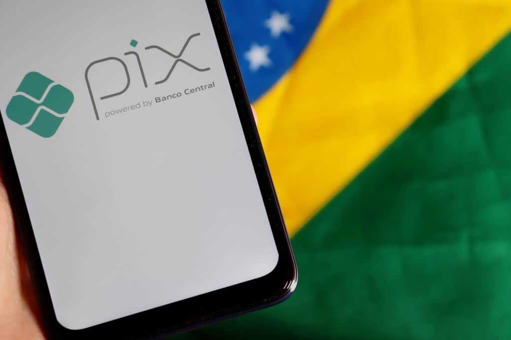 Pix parcelado tem lançamento adiado pelo BC, diz jornal Nesta sexta-feira (26), o Banco Central (BC) adiou o lançamento do Pix parcelado, modalidade de pagamento que seria lançada ainda este mês, segundo informações do O GLOBO e confirmadas pela Folha de S.Paulo. Ao fundo, bandeira do Brasil; à frente, smartphone exibindo, em sua tela, o logo do Pix