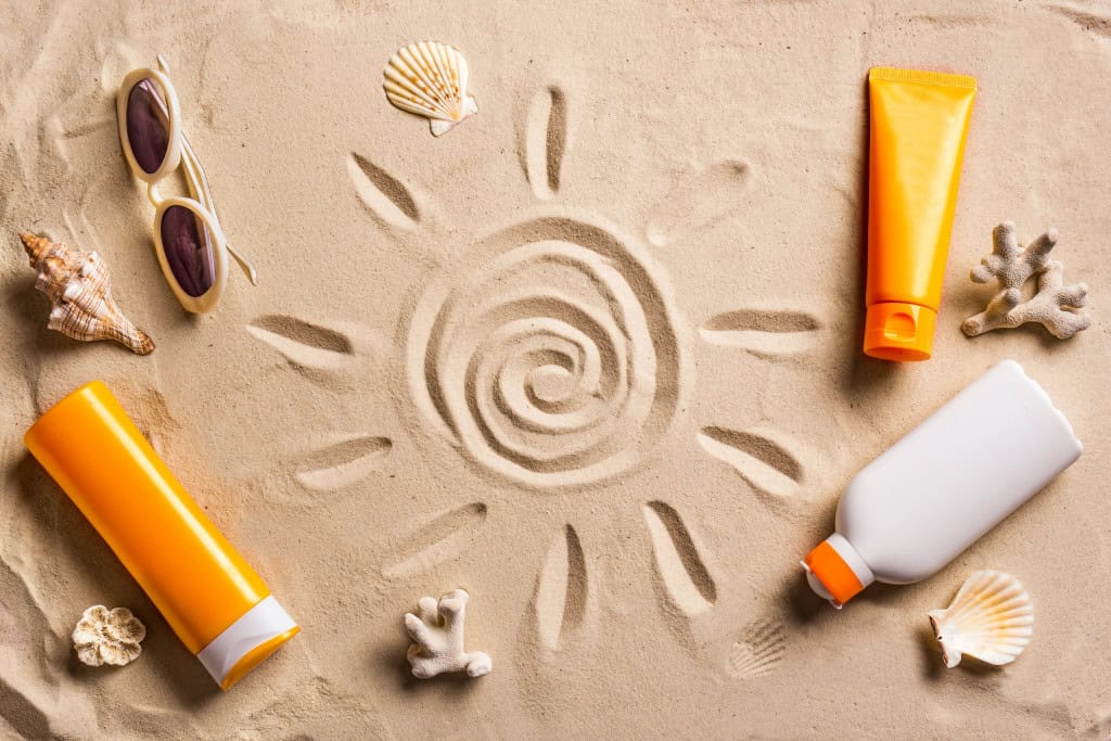 Escândalo do protetor solar na Austrália: isso pode acontecer no Brasil? Imagine que você usa um protetor solar religiosamente para evitar as fortes incidências de raios solares durante o dia. Desenho do Sol feito na areia e com vários tipos de protetores solares ao redor