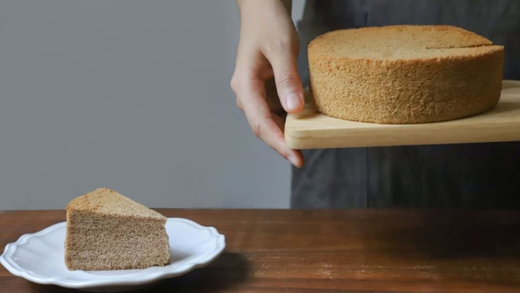 Pessoa segurando uma tábua com bolo, ao lado de pedaço de bolo sobre um prato