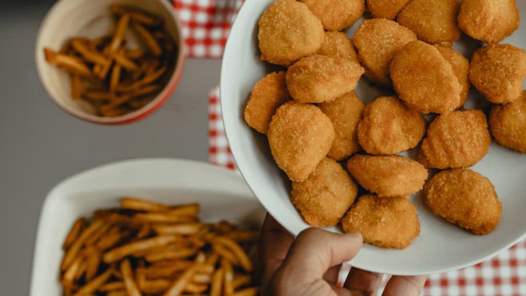 Mão segurando um prato de fritura, com batatas fritas ao fundo