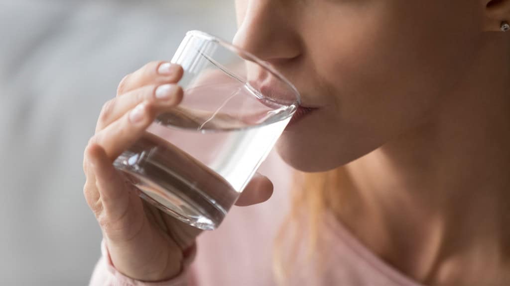 10 sinais que mostram que você está desidratado e quando buscar ajuda médica Na rotina intensa do dia a dia, é muito comum que nos esqueçamos de algo básico para a nossa saúde: beber água. A hidratação é essencial para regular a temperatura corporal, manter a circulação sanguínea, auxiliar na digestão e garantir o bom funcionamento das células. Close-up de mulher com sede segurando um copo e bebendo água para evitar a desidratação e manter o equilíbrio do corpo
