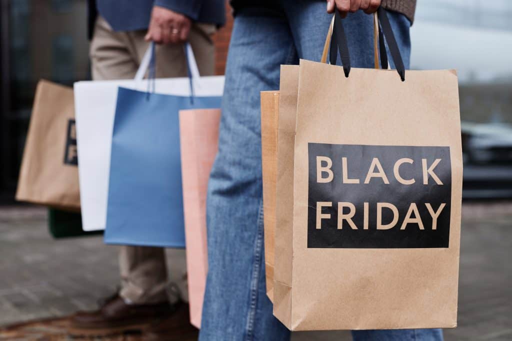 Sacolas nas mãos de pessoas; uma delas tem a inscrição "Black Friday"