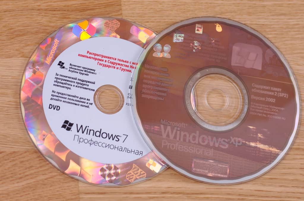 Dois CDs de instalação do Windows, sendo o da esquerda do Windows 7 e, o da direita, do XP, que está parcialmente por cima do primeiro
