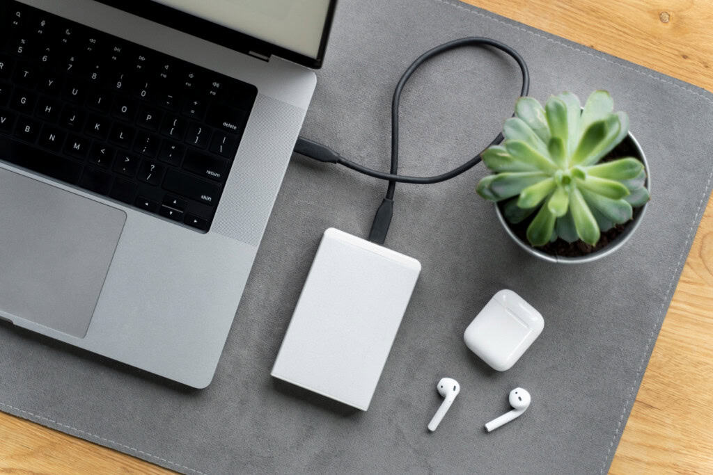 6 dicas para escolher o power bank perfeito para você Ficar sem bateria no meio do dia é um problema que quase todo mundo já enfrentou. Seja durante uma viagem, no trabalho ou em um passeio, não há nada pior do que ver o celular desligando quando você mais precisa dele. notebook sendo carregado em um power bank com fones de ouvido do lado