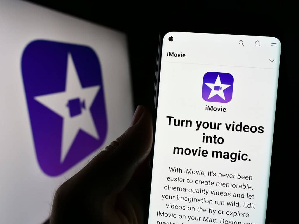 5 alternativas ao Clips para edição de vídeo no iPhone A Apple encerrou oficialmente o suporte ao Clips, seu aplicativo gratuito de edição de vídeo. A decisão, que pegou de surpresa quem usava o app para criar vídeos rápidos e criativos, abre espaço para ferramentas mais completas com recursos profissionais, maior controle e resultados de qualidade. Imagem mostra pessoa segurando um celular com o site do software de edição de vídeo iMovie (Apple Inc.) na tela, em frente ao logotipo