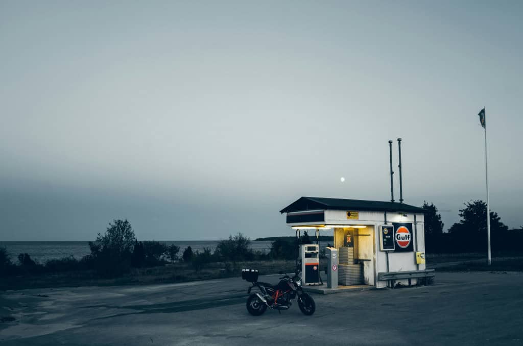 Imagem mostra posto de gasolina ao anoitecer, com a moto parada