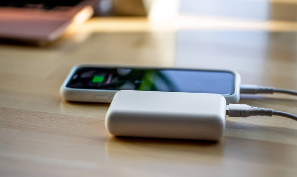 6 dicas para escolher o power bank perfeito para você Ficar sem bateria no meio do dia é um problema que quase todo mundo já enfrentou. Seja durante uma viagem, no trabalho ou em um passeio, não há nada pior do que ver o celular desligando quando você mais precisa dele. celular sendo carregado power bank