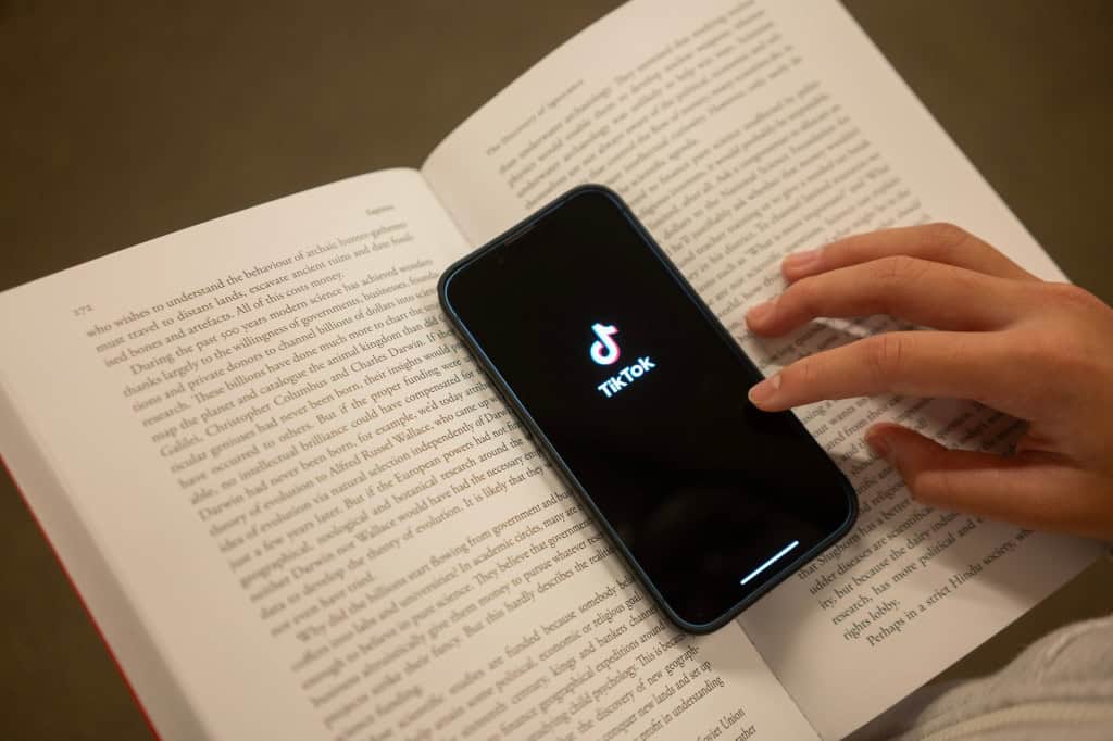 Perde a noção do tempo no TikTok? Entenda mecanismo que causa isso Um estudo conduzido pelo The Washington Post revelou detalhes sobre como o TikTok consegue manter seus usuários conectados por horas todos os dias. O jornal analisou o comportamento de 1,1 mil pessoas, com base em um banco de dados de cerca de 15 milhões de vídeos assistidos ao longo de seis meses, mostrando o quão eficaz é o algoritmo da plataforma em criar hábitos de uso. Smartphone com logo do TikTok em cima de um livro