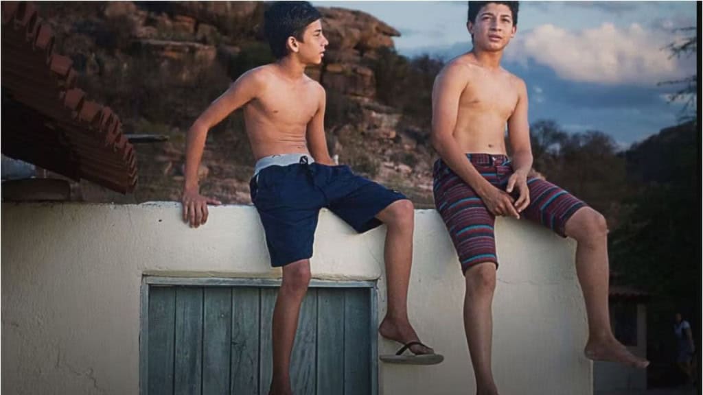 Dois meninos de bermuda e sem camisa, sentados em cima de um muro de uma casa no nordeste