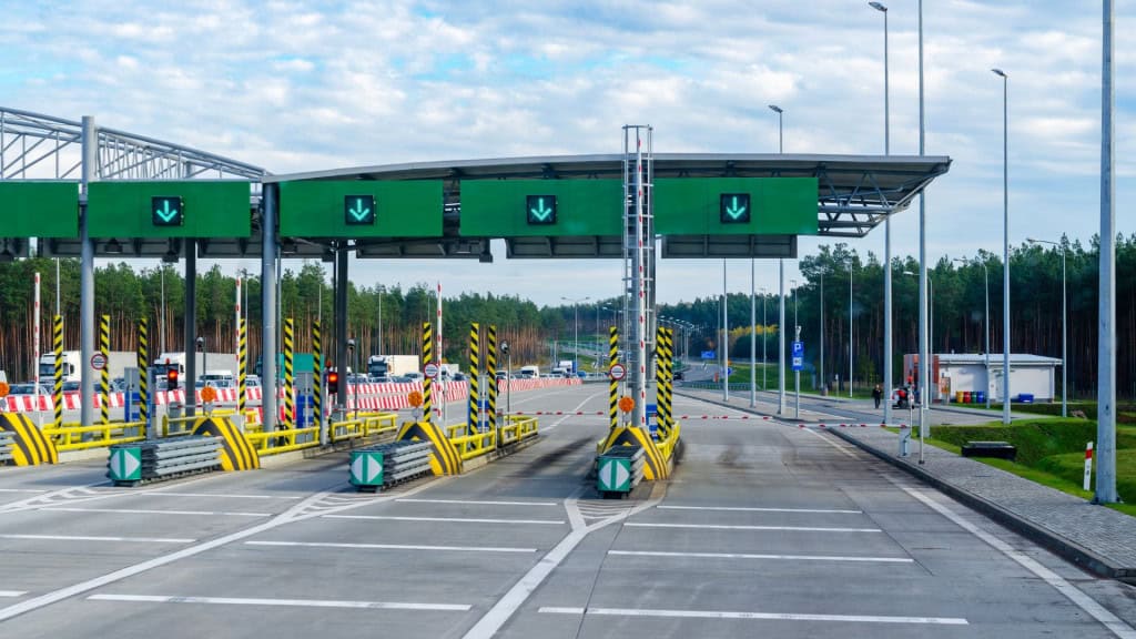 Idoso tem desconto no pedágio ou está isento de cobrança? Nos últimos dias, circulou nas redes sociais a informação de que motoristas idosos não precisariam mais pagar pedágios nas rodovias brasileiras. A notícia se espalhou rapidamente e gerou muitas dúvidas: será que essa medida já está valendo? É um direito garantido por lei ou apenas uma proposta em discussão? Cabines de pedágio com várias faixas abertas e sinalização verde, onde carros aguardam passagem em uma estrada cercada por árvores.