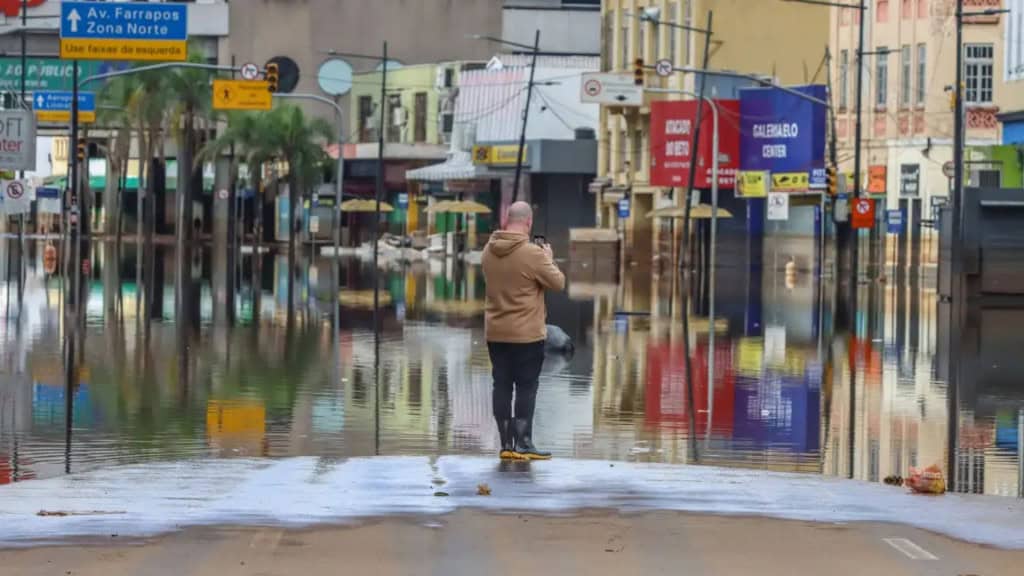 Homem tirando foto com celular de avenida alagada no Rio Grande do Sul
