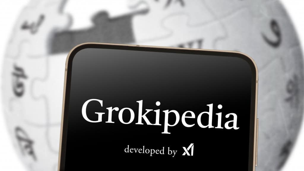 Celular com logomarca da Grokipedia na tela colocado na frente de monitor exibindo imagem do logotipo da Wikipedia