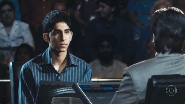 Menino participando de programa de Tv de perguntas e respostas, esta sentado na frente do apresentador