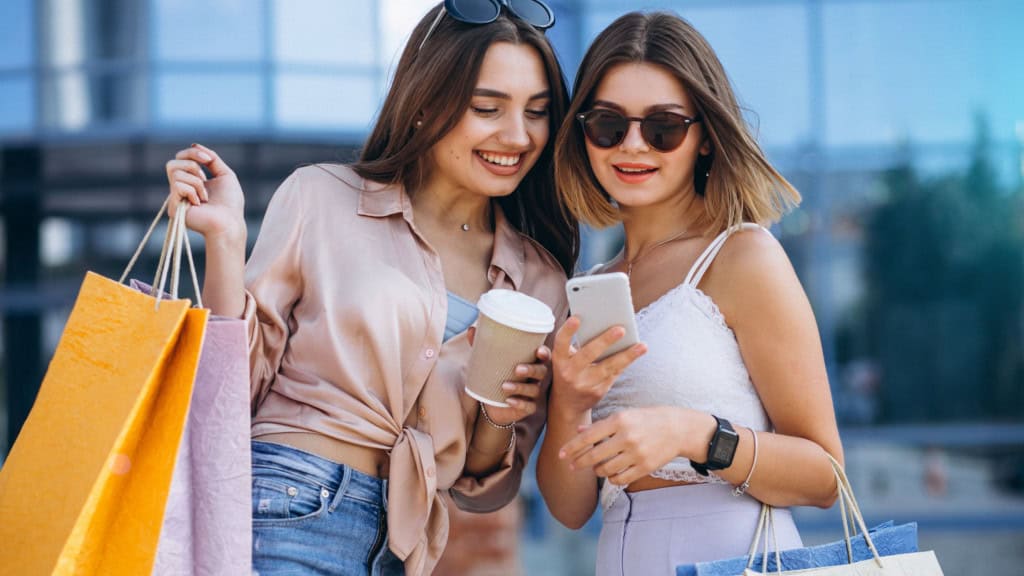 duas garotas com sacolas de compras animadas, olham o celular