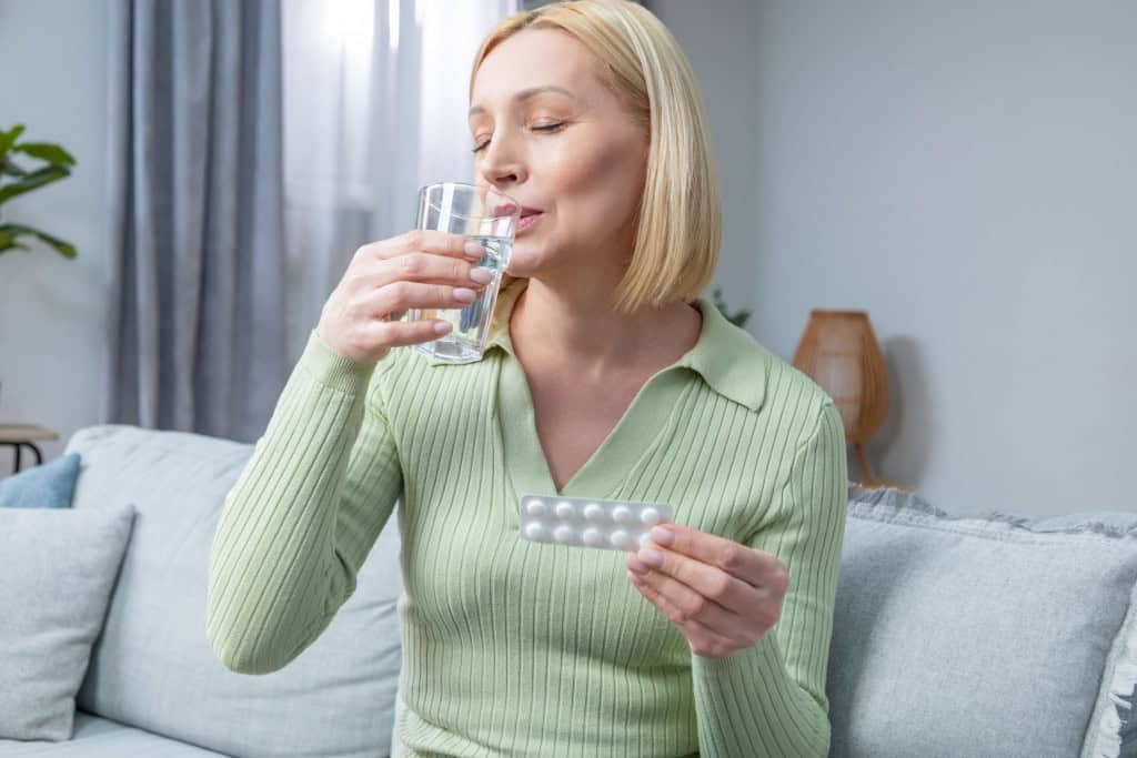 Mulher toma medicamento com água enquanto segura uma cartela do remédio
