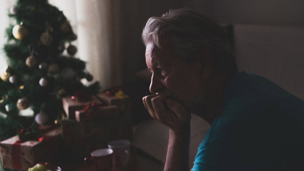 Idosa com mão embaixo do queixo com olhar triste e árvore de natal ao fundo