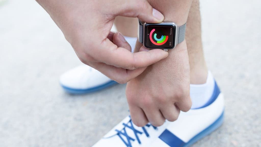 mão masculina com braço abaixado em direção aos pés, ativando seu apple watch antes de correr, o homem usa tênis de corrida.