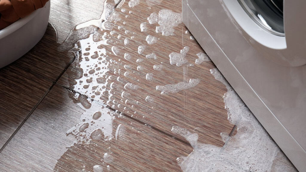 Aguá com espuma de sabão saindo embaixo da máquina de lavar