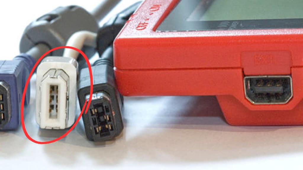 Três cabos antigos ao lado de um console, cabo FireWire 400 em destaque dentro de círculo vermelho