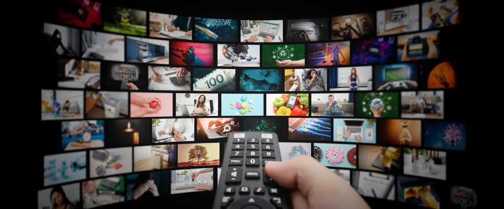 Várias janelas de streaming abertas; à frente, uma mão segurando um controle