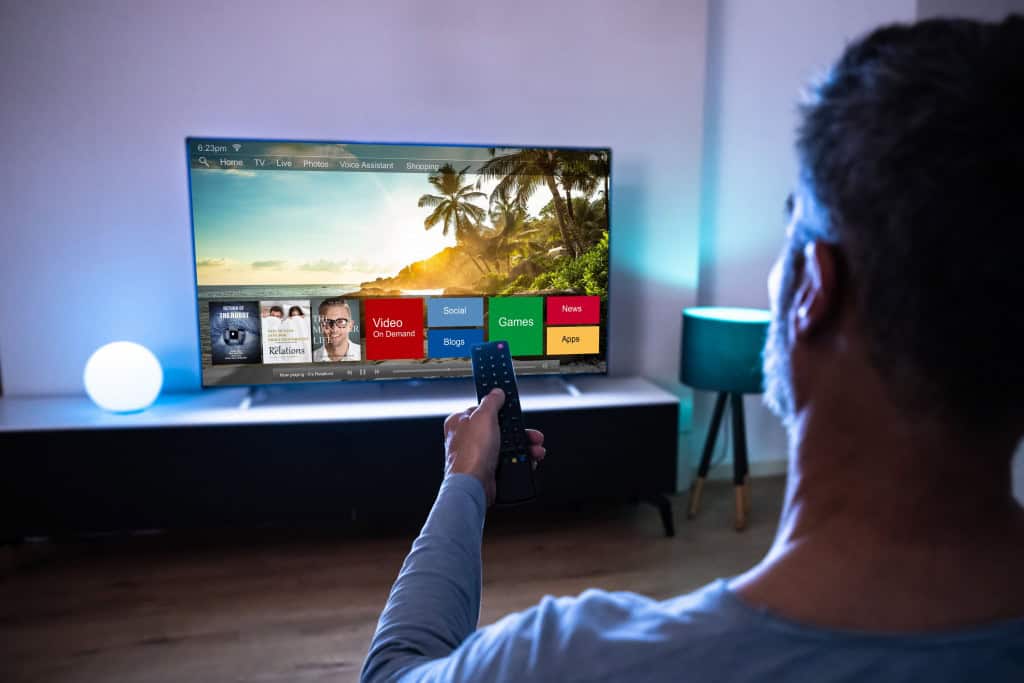 Imagem mostra pessoa assisntidno TV com o controle na mão para selecionar opção de streaming
