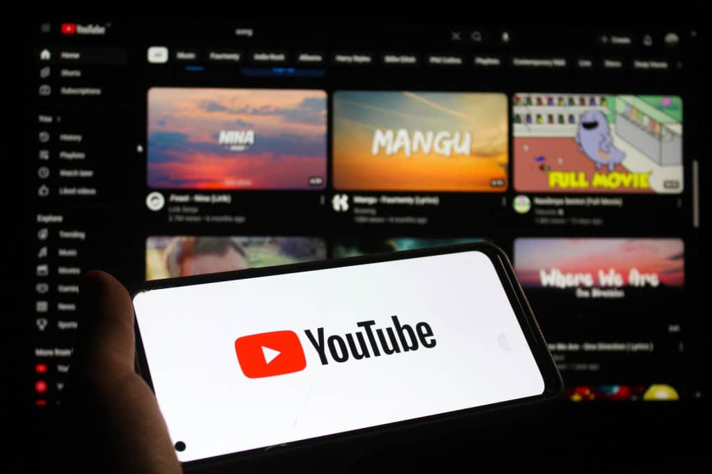 Ao fundo, página web do YouTube; à frente, logo do YouTube em um smartphone na horizontal