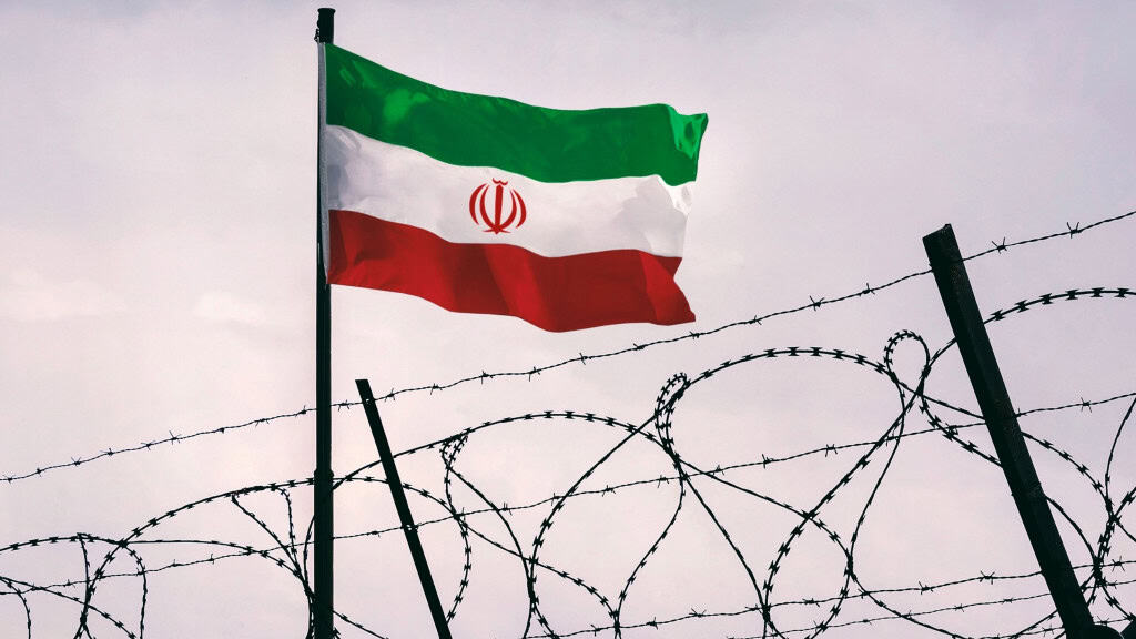 Bandeira do Irã hasteada atrás de cerca de arame farpado
